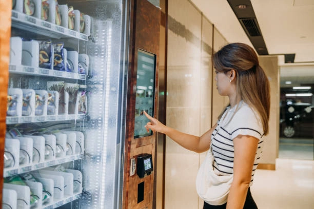 An Asian woman using a modern vending machine to buy food and drink in store.